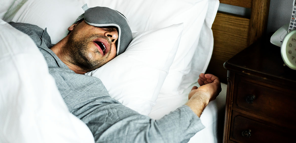 man sleeping in bed with face mask on while snoring
